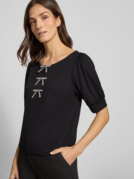 Vrouwenmodel draagt Sweatshirt met Puffärmeln und Schleifen-Applikationen van monari, zwart, halve mouw, ronde hals, viscosemix, regular fit, detailopname bovenlichaam.