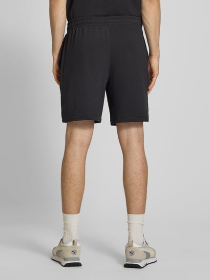 Männermodel trägt Shorts mit Logo-Stitching von PUMA PERFORMANCE in Schwarz mit Strukturmuster aus Reine Baumwolle, Gerader-Schnitt, Elastischer-Bund, Ganzkörperansicht Rückansicht.