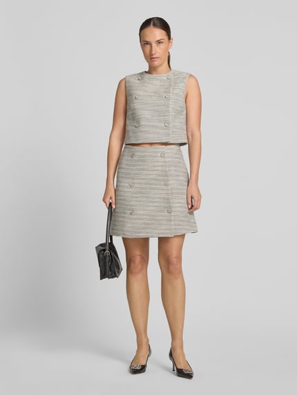 Frauenmodel trägt eng anliegenden Mini-Rock mit doppelreihiger Knopfleiste Modell 'RALINEA' von HUGO in Grau-Beige-Tönen, Ganzkörperansicht von vorne, Damen Mini-Rock von HUGO.