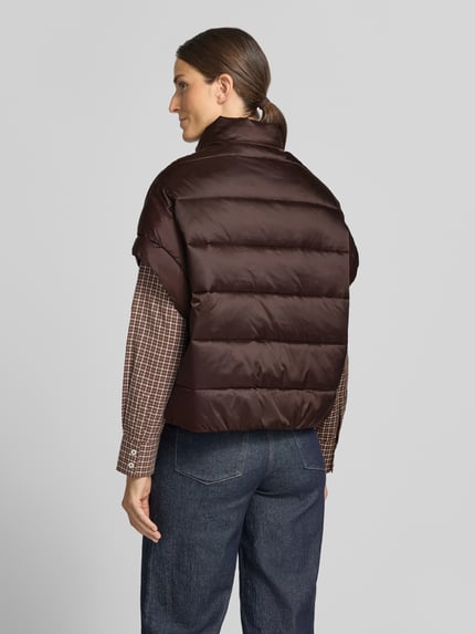 Frauenmodel trägt Steppweste mit Stehkragen und Eingrifftaschen von Milano Italy in Braun, glänzende Oberfläche, lockerer Schnitt, Ganzkörperansicht Rückansicht. Rückenlänge 59 cm, Schulterbreite 50 cm, Brustweite 63 cm.