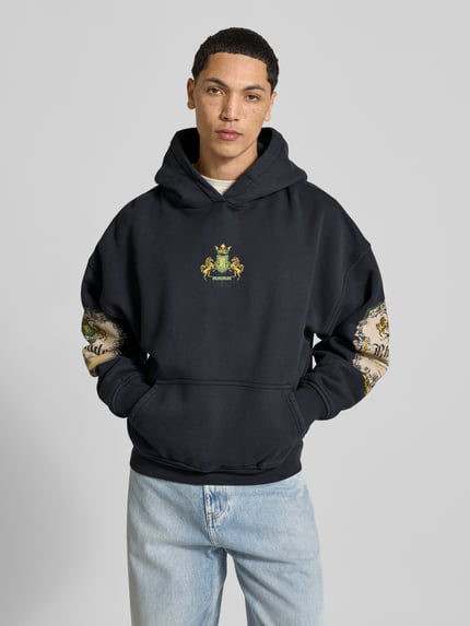 Mannermodel draagt Oversized Hoodie uit pure katoen van RHUDE met labelprint, kangoeroezak en ribboorden, heren, vooraanzicht bovenlichaam. Ruglengte bij maat M: 63 cm.