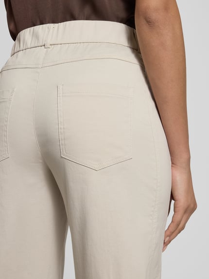 Frauenmodel trägt Straight Fit Stoffhose mit Eingrifftaschen Modell 'Ornela' von STEHMANN aus elastischem Baumwoll-Mix in Beige, Detailaufnahme Rückansicht.