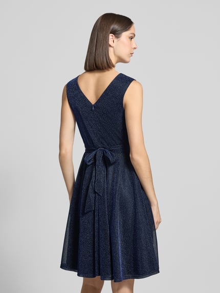 Vrouwenmodel draagt knielanges Kleid in Wikkellook van Apricot, getailleerd, v-hals, tailleband, mouwloos, onderrok, glitterlook, ruglengte maat S 93 cm, borstwijdte maat S 32 cm, donkerblauw met lichte glans, lichte A-lijn, textuur fijne glitterstructuur, helemaal van achteren gezien.