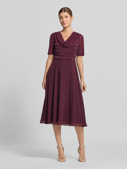 Kobiece model prezentuje Fit and Flare Cocktailkleid mit Wasserfallausschnitt od Vera Mont, sukienka koktajlowa w kolorze bordowym, gładka tekstura, cała sylwetka z przodu.