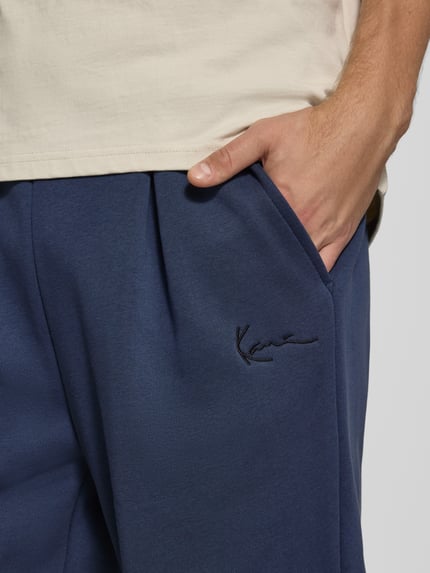Männermodel trägt Sweatpants mit Logo-Stitching und Eingrifftaschen von Karl Kani in Dunkelblau, Baumwoll-Mix, Nahaufnahme Oberkörper.