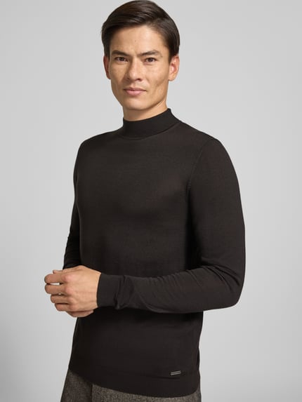 Männermodel trägt gebreide pullover uit zuivere scheerwol met opstaande kraag van ROY ROBSON, slim fit, labeldetail, ruglengte maat M 73 cm, mouwlengte maat M 73 cm, donkere effen kleur, gladde textuur, Ganzkörperansicht van voren.