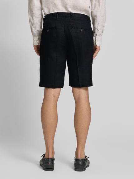 Männermodel trägt Shorts aus Leinen mit Eingrifftaschen von MARKUP, schwarze Farbe, Straight Fit, Ganzkörperansicht Rückansicht. Bundweite 22 cm, Innenbeinlänge 34 cm, Gesäßleistentaschen mit Knopfverschluss.