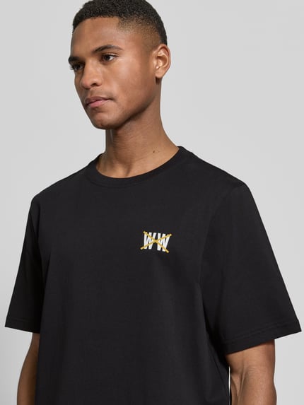 Männermodel trägt Regular Fit T-Shirt mit Logo-Print Modell 'Bobby' von Wood Wood in Schwarz aus reiner Baumwolle, Nahaufnahme Oberkörper.