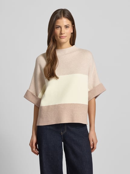 Frauenmodel trägt Strickpullover mit Stehkragen von More & More im Viskose-Mix, lockerer Schnitt, helle Creme- und Beigetöne, Ganzkörperansicht von vorne.