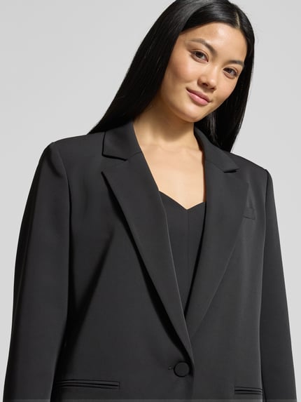 Vrouwenmodel draagt Relaxed Fit Blazer met Paspeltaschen van Jake*s Cocktail, zwart met reverskraag en knoopsluiting, Nahaufnahme bovenlichaam.