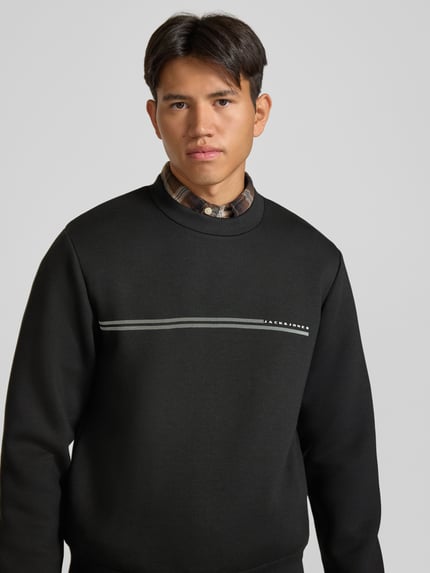 Männermodel trägt Relaxed Fit Sweatshirt mit Viskose-Anteil Modell 'Fusion' von JACK & JONES, Schwarz, Logo-Print, Nahaufnahme Oberkörper, Material-Mix mit Viskose-Anteil.