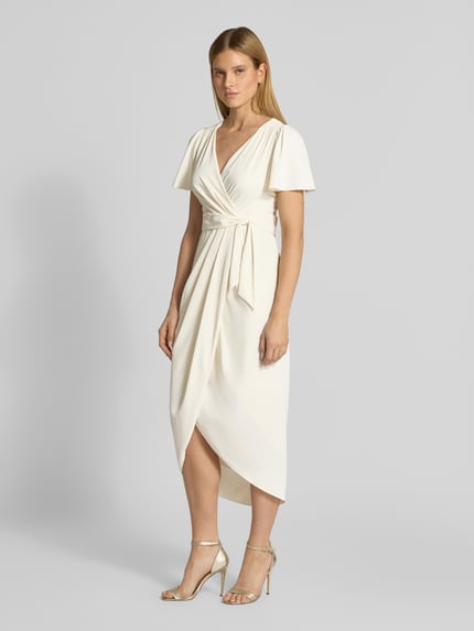 Vrouwenmodel draagt Cocktailkleid in Wickel-Optik met Schmetterlingsärmeln van Christian Berg Cocktail in ecru satijnlook, getailleerd model, midi-jurk, v-hals, strikceintuur, verlengde rug, haakjes- en ritssluiting, ruglengte maat 36: 133 cm, borstwijdte: 40 cm, mouwlengte: 24 cm, geheel in beeld, vooraanzicht.