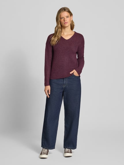 Vrouwenmodel draagt Regular Fit Pullover met V-hals model 'CAMILLA' van ONLY in bordeauxrood, gecombineerd met blauwe denim broek en sneakers, damespullover von ONLY, volledige lichaamsvoorzijde