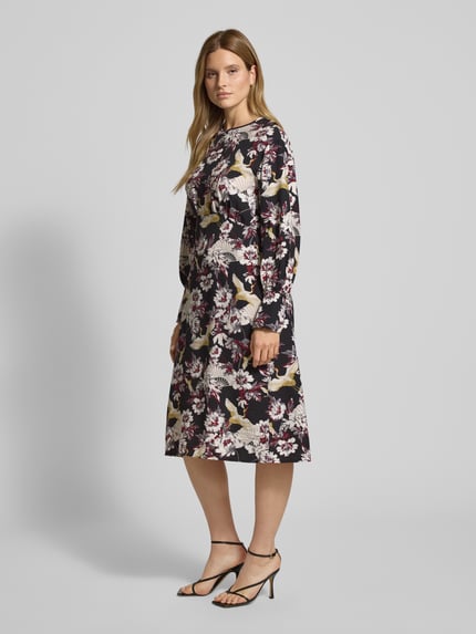 Kobiece model nosi Midikleid mit Rundhalsausschnitt Modell 'Orelia' od GUIDO MARIA KRETSCHMER WOMAN, czarna tkanina z kwiatowym wzorem, luźny krój, długość midi, perspektywa całego ciała z przodu.