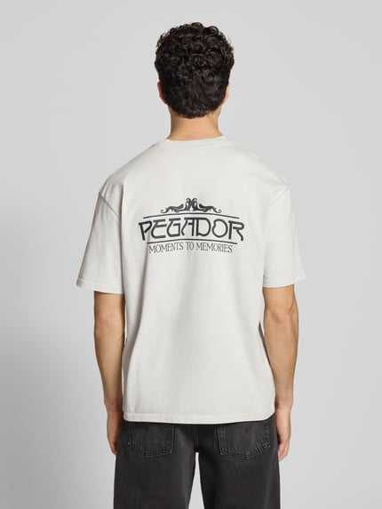 Męski model nosi Oversized T-Shirt aus Baumwolle Modell 'Stavoren' von Pegador, bawełna, krój oversize, biały, nadruk, półrękaw, widok całej sylwetki z tyłu.