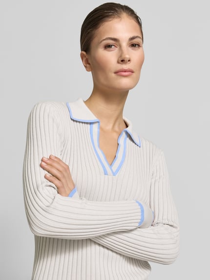 Vrouwenmodel draagt Geripptes Longsleeve mit V-Ausschnitt - curated by Tinvcb van SIC, beige ribtextuur, slim fit, resortkraag, V-hals, puur katoen, details in lichtblauw, Nahaufnahme bovenlichaam.