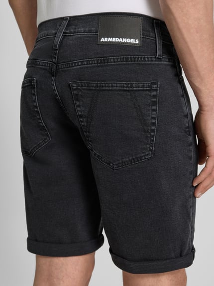 Männermodel trägt Slim Fit Jeansshorts aus katoenmix Modell 'NAAILO' van Armedangels in denimlook met labelpatch, 5-pocketmodel, omslag aan de pijpen, ritssluiting en riemlussen, detailaufnahme achterzijde.