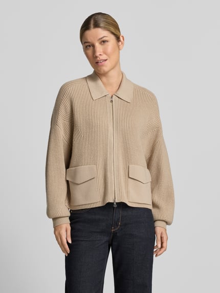 Frauenmodel trägt Strickjacke aus Schurwolle mit Pattentaschen von windsor., beige Farbton, Umlegekragen, Zweiwege-Reißverschluss, Relaxed Fit, gerippte Textur, Ganzkörperansicht von vorne.