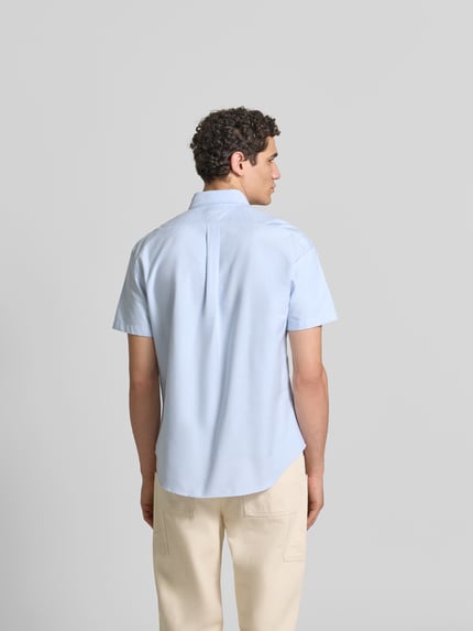 Męski model nosi Slim Fit Freizeithemd mit Logo-Stitching od Kenzo z bawełny, kołnierzyk typu button down, krótki rękaw, krój slim fit, szerokość ramion w rozmiarze M 77 cm, długość tyłu 49 cm, długość rękawów 29 cm, jasnoniebieska, gładka tekstura, całkowity widok z tyłu.