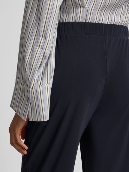 Frauenmodel trägt Relaxed Fit Stoffhose mit Tunnelzug von MM by Max Mara, dunkle Farbe, glatte Textur, Detailaufnahme Rückenansicht, Damen Stoffhose mit Gürtelschlaufen und Eingrifftaschen.