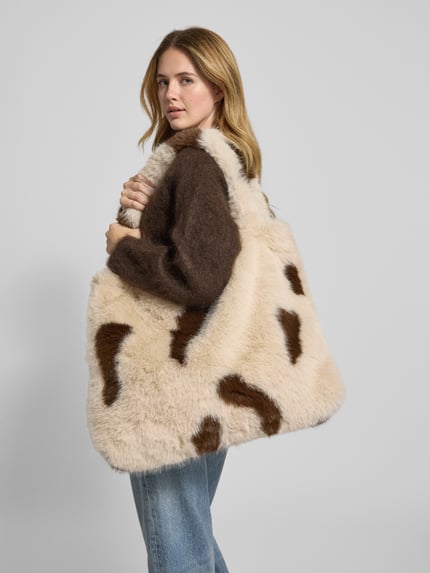 Frauenmodel trägt Mom Bag aus Kunstfell mit Allover-Animal-Print von STUDIO NOOS in Beige und Braun, Tragehenkel, offene Struktur, Ganzkörperansicht von vorne. Breite 55 cm, Länge 40 cm, Tiefe 10 cm, Schulterriemen 70 cm.