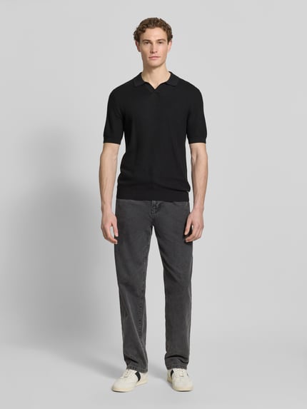 Männermodel trägt Slim Fit Poloshirt mit Viskose-Anteil von Roy Robson in Schwarz mit Strick-Optik, Strukturmuster und elastischen Abschlüssen, Rückenlänge bei Größe M: 67 cm, Ärmellänge 27 cm, Ganzkörperansicht von vorne.