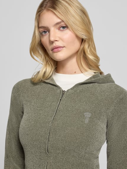 Frauenmodel trägt Sweatjacke mit Kapuze Modell 'MAYA KNIT HOODIE' von Juicy Couture, unifarben, Strickoptik, Logo-Stitching, Nahaufnahme Oberkörper.