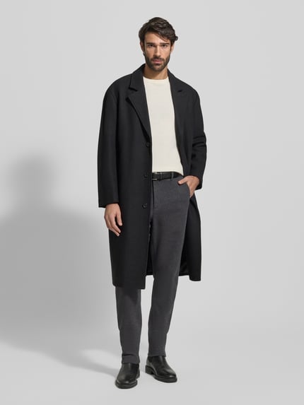 Männermodel trägt Relaxed Fit Schmale Hose aus reiner Baumwolle Modell 'HARLEM' von Tommy Hilfiger in Optik: Unifarben Two-Tone, Label-Stitching-Applikation, Logo-Details, Gürtelschlaufen, Knopf und verdeckter Reißverschluss, Bundabschluss: elastisch, Gesäßtaschen, seitliche Eingrifftaschen, Material: reine Baumwolle; schmale, gerade Form und glatte Textur, dunkle Farbtöne, Ganzkörperansicht von vorne.