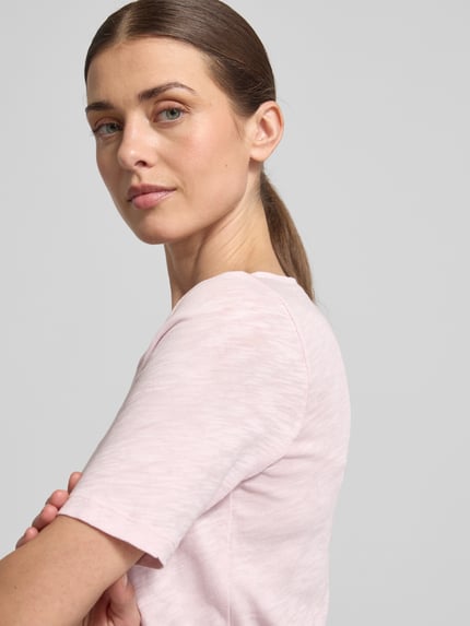 Frauenmodel trägt Slim Fit T-Shirt aus reiner Baumwolle von Marc O'Polo, unifarben Melange in Hellrosa, Logo-Print, Nahaufnahme Oberkörper.