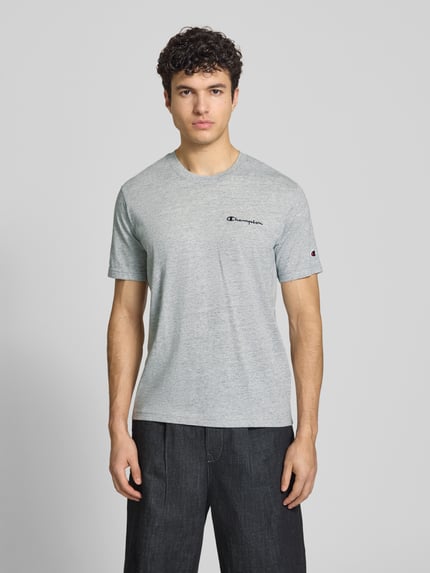 Männermodel trägt graues Herren T-Shirt mit Logo-Stitchings Modell 'ICONS CONTRAST' von CHAMPION aus Baumwoll-Mix, Modern Fit, Rundhalsausschnitt, Rückenlänge 70 cm bei Größe M, Ganzkörperansicht von vorne.