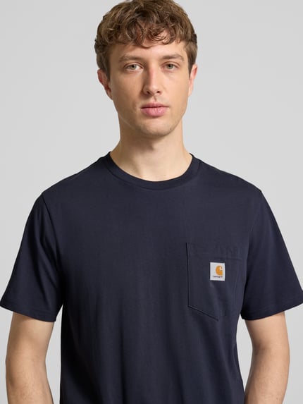 Männermodel trägt Regular Fit T-Shirt mit Logo-Patch von Carhartt Work In Progress aus reiner Baumwolle in Dunkelblau, Nahaufnahme Oberkörper.