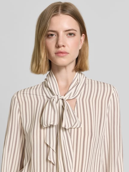 Frauenmodel trägt Slim Fit Schluppenbluse aus Viskose von Comma mit braunen Streifen, Teilungsnaht, Sportmanschetten, Nahaufnahme Oberkörper. Rückenlänge bei Größe 36: 64 cm, Ärmellänge 63 cm.