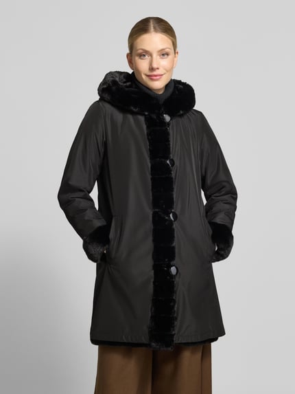 Frauenmodel trägt Regular Fit Mantel mit Wendefunktion und Webpelz-Innenseite von PETITE M., schwarze Optik, schlichtes Design, Ganzkörperansicht von vorne. Rückenlänge 85 cm, Schulterbreite 39 cm, Brustweite 50 cm, Ärmellänge 62 cm.