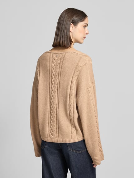 Frauenmodel trägt Pullover aus Schurwolle mit Zopfmuster von BOSS Orange, unifarben, strukturierte Strickoptik, Ganzkörperansicht Rückansicht.