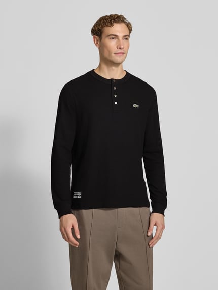 Männermodel trägt Regular Fit Langarmshirt aus reiner Baumwolle von Lacoste, Farbe Schwarz, glatte Struktur, Ganzkörperansicht von vorne. Herren Langarmshirt von Lacoste.