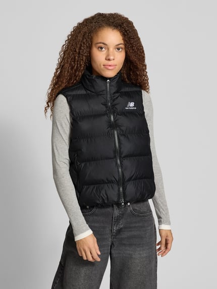 Frauenmodel trägt Steppweste mit Stehkragen Modell 'BOSTON PUFFER VEST' von NEW BALANCE, unifarben schwarz, Struktur, Logo-Print, Ganzkörperansicht von vorne