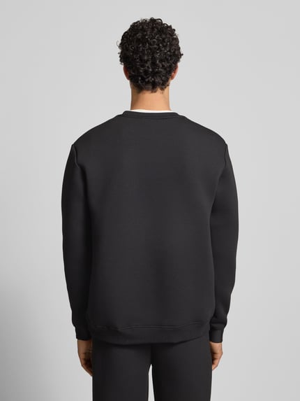 Männermodel trägt zwart Sweatshirt met label-print, losse pasvorm, geribbelde boorden, ronde hals, model 'CORVARO' van Ellesse, materiaal-mix met viscose, ruglengte 69 cm, mouwlengte 64 cm, geheel effen, textuur glad, ganzkörperansicht rückansicht.