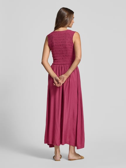 Vrouwenmodel draagt maxi-jurk uit viscosemix met smokdetail, A-lijn, model 'Sorellia' van mbyM, ruglengte maat S 130 cm, borstwijdte 36 cm, effen donkerroze, gladde textuur, geheel beeld van achteren.