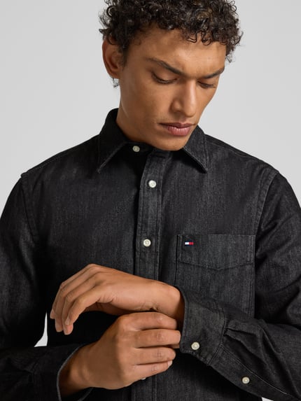 Männermodel draagt Regular Fit Jeanshemd uit puur katoen van Tommy Hilfiger in black denimlook met kentkraag, borstzak en labeldetail, nahaufnahme bovenlichaam.