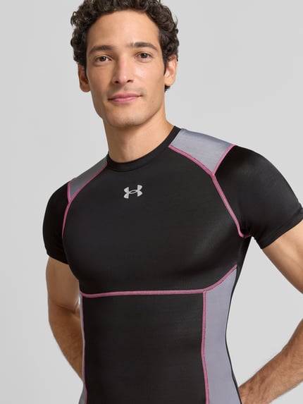 Mężczyznamodel nosi Slim Fit Sport-T-Shirt mit Kontrastnähten Modell 'HeatGear®' von Under Armour, czarny z szarymi panelami i różowymi szwami, Herren Sport-T-Shirt von Under Armour, zbliżenie na górną część ciała