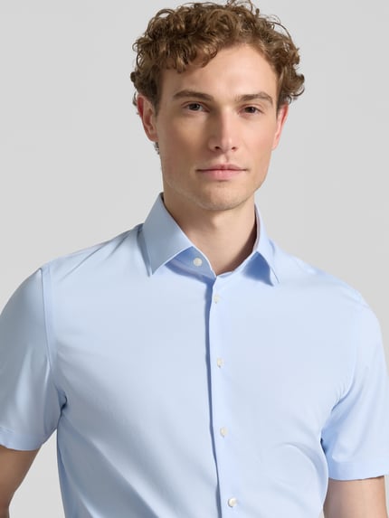 Männermodel trägt Slim Fit Business-Hemd mit Kentkragen von Jake*s in Hellblau, Elastischer-Material-Mix, Knopfleiste, Kurzärmelig, Nahaufnahme Oberkörper.