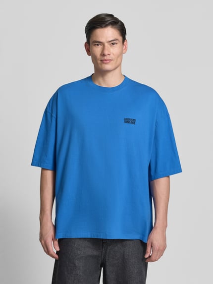 Männermodel trägt Herren T-Shirt mit Logo-Print, Modell 'GIXY' von American Vintage, kräftiges Blau, Reine Baumwolle, Loose-Fit, Rundhalsausschnitt, überschnittene Schultern, Rückenlänge bei Größe M/L: 72 cm, Ganzkörperansicht von vorne.