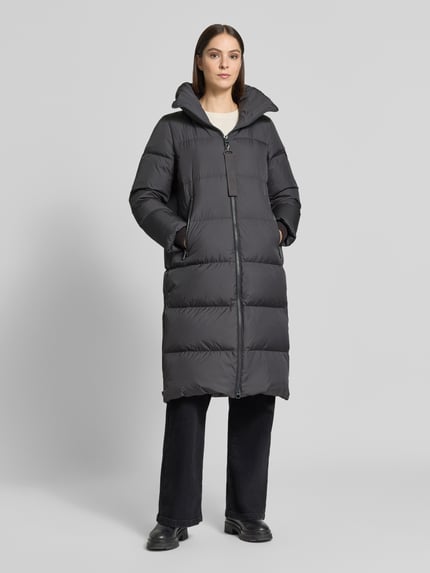 Frauenmodel trägt Regular Fit Daunenmantel mit abnehmbaren Rucksackriemen von Marc O'Polo, dunkler Farbton, glatte Oberfläche, Ganzkörperansicht von vorne. Damen Daunenmantel von Marc O'Polo.