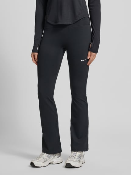 Frauenmodel trägt Flared Cut Leggings mit Logo von NIKE TRAINING aus schwarzem Material-Mix mit Stretch-Anteil, elastischer Bund, Logo, Nahaufnahme Unterkörper.