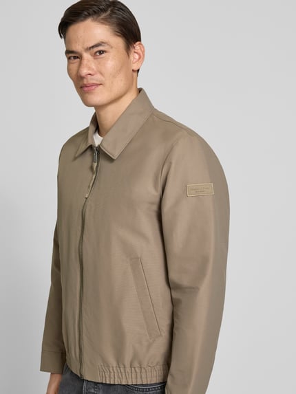 Mannenmodel draagt Regular Fit blouson met elastische rompzoom van Marc O'Polo, look: effen, platte kraag, ritssluiting, labelpatch, lange mouw, drukknoop, steekzakken, binnenzak, regular fit pasvorm, zijaanzicht bovenlichaam.