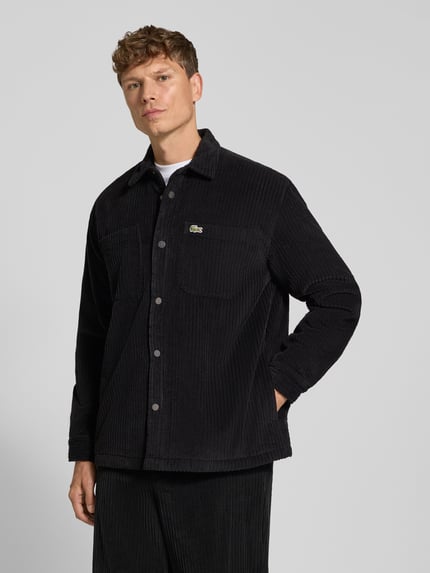 Männermodel trägt Regular Fit Hose mit seitlichen Eingrifftaschen von Lacoste in schwarzer Cord-Struktur, unifarben, Ganzkörperansicht von vorne.