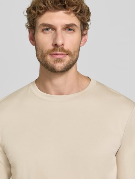 Männermodel trägt Regular Fit Longsleeve aus reiner Baumwolle Modell 'Pima' von RAGMAN in Beige, glatte Textur, Nahaufnahme Oberkörper. Rückenlänge bei Größe M 69 cm, Rundhalsausschnitt.