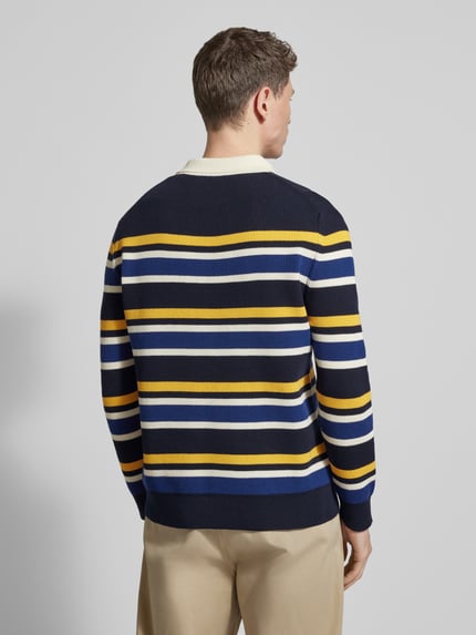 Męski model nosi Strickpullover mit Polokragen und Label-Patch od Gant, bawełniana mieszanka, prosty krój, granatowy z żółtymi i białymi paskami, długość tyłu w rozmiarze M: 68 cm, długość rękawa w rozmiarze M: 66 cm, widok całej sylwetki z tyłu.