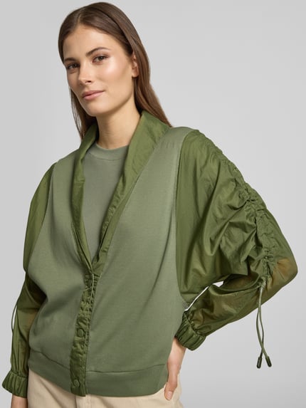 Vrouwenmodel draagt Relaxed Fit Leichte Jacke im Material-Mix van Marc Cain, look: effen, pasvorm: relaxed fit, sjaalkraag, plooien, verdekte knoopsluiting, mouwvorm: 3/4-mouw, materiaalverwerking: satijn en chiffon, materiaal: katoenmix. Nahaufnahme bovenlichaam.