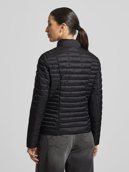 Modelka nosi Kurtka pikowana z zamkiem błyskawicznym dwustronnym model 'JUDY' od Frieda & Freddies, kolor czarny, krój slim fit, stójka, kieszenie zapinane na zamek błyskawiczny, długość tyłu w rozmiarze 36: 57 cm, szerokość ramion w rozmiarze 36: 40 cm, szerokość klatki piersiowej w rozmiarze 36: 48 cm, długość rękawów w rozmiarze 36: 64 cm, widok całej sylwetki od tyłu.